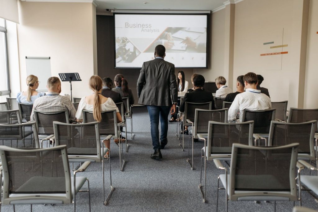 a-man-walking-on-aisle-between-chairs-with-people-sitting