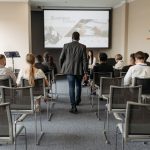 a-man-walking-on-aisle-between-chairs-with-people-sitting